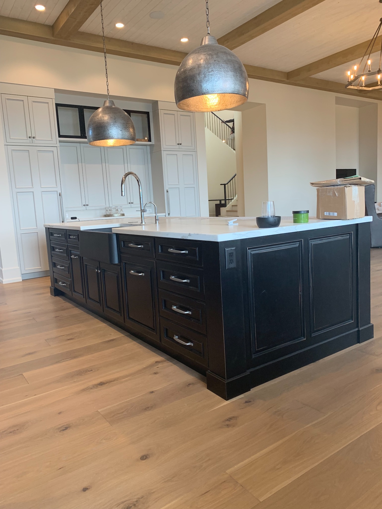 Large black kitchen island with raised-panel cabinetry, farmhouse sink, and white stone counter
