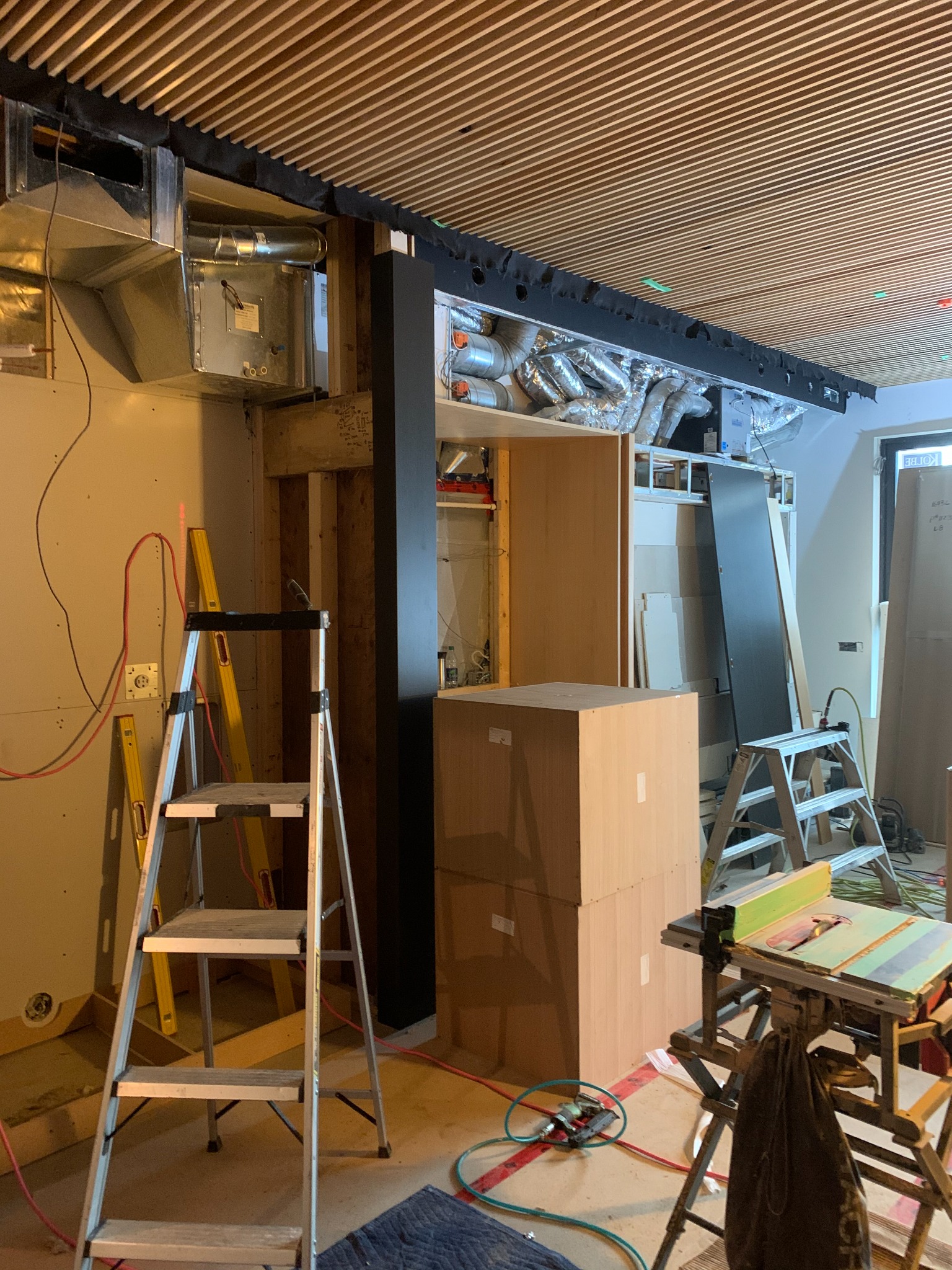 Commercial millwork installation in progress beneath a wood-slat ceiling